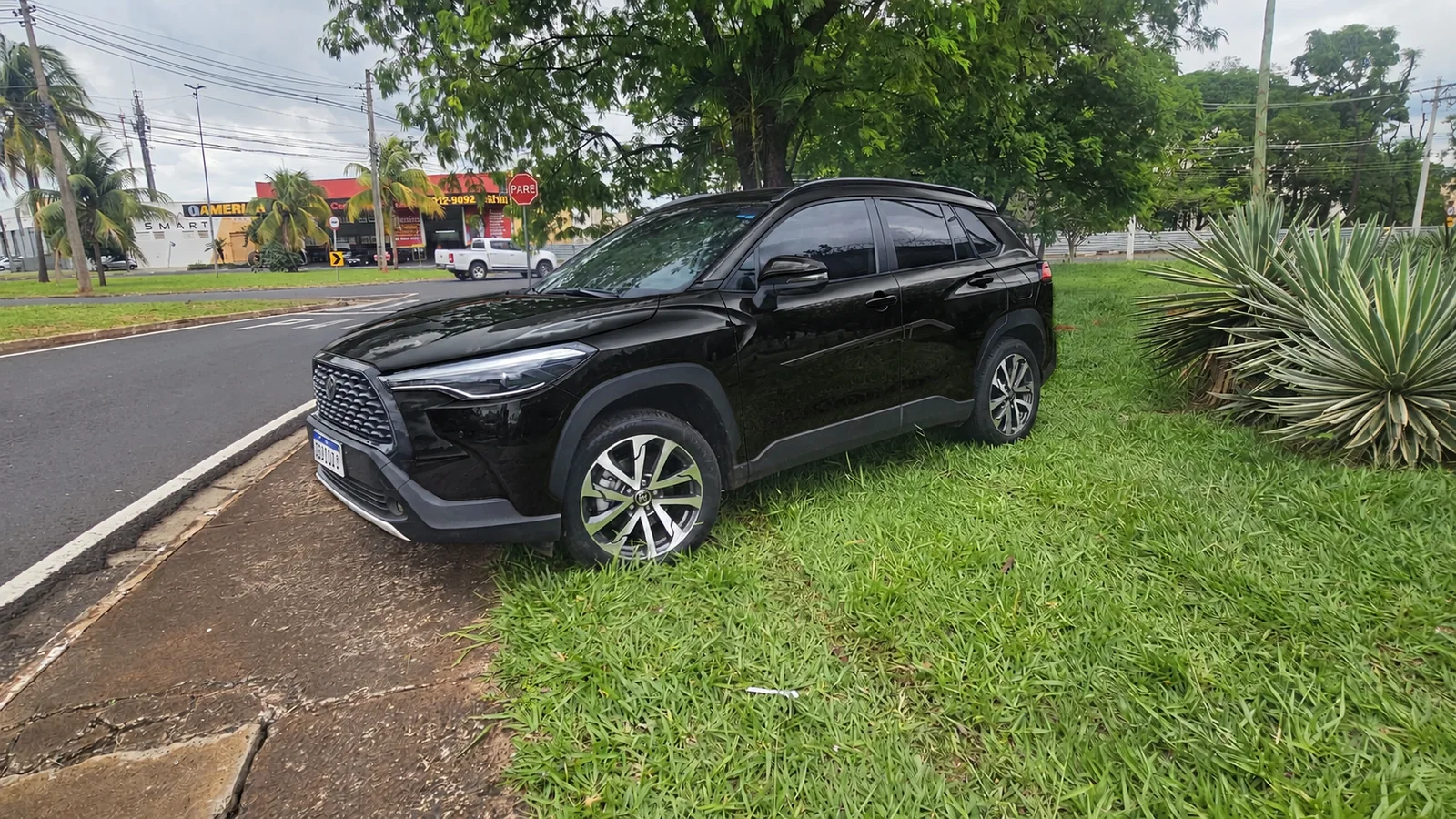 Toyota Corolla Cross preto estacionado em área verde, visto de frente e de lado.